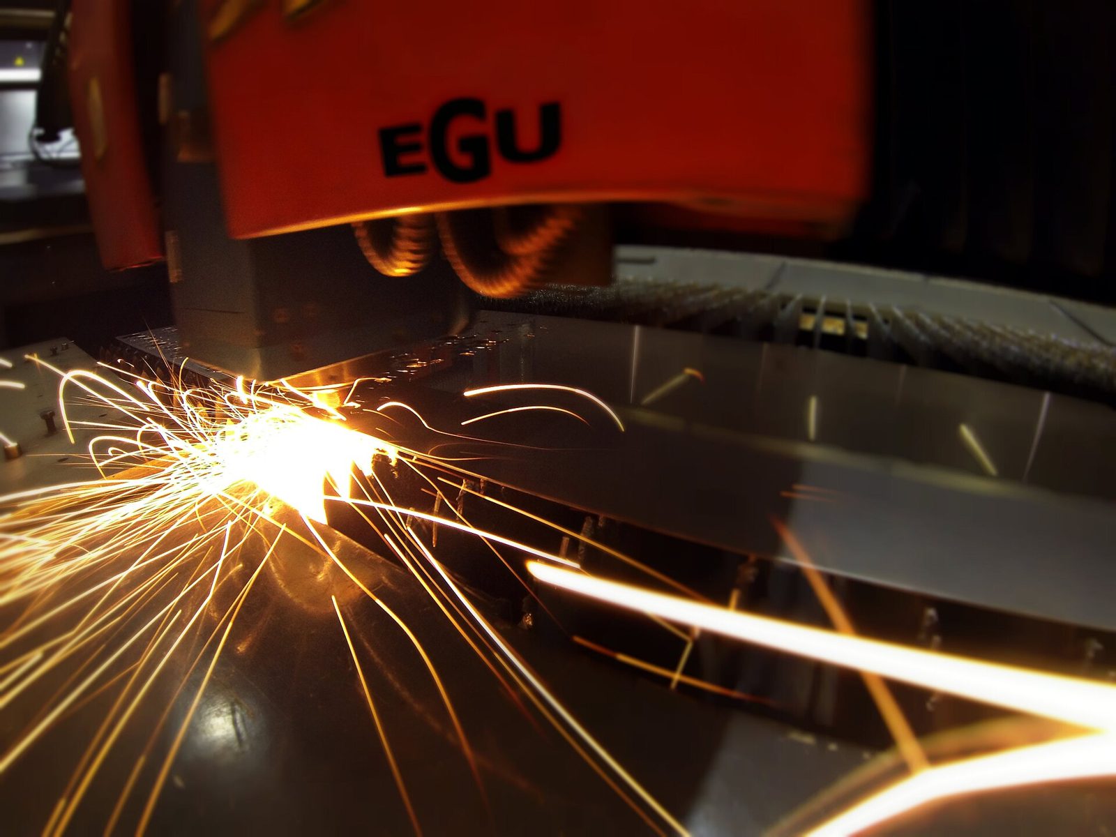 Illustrative laser cutting head slicing through sheet steel with bright sparks