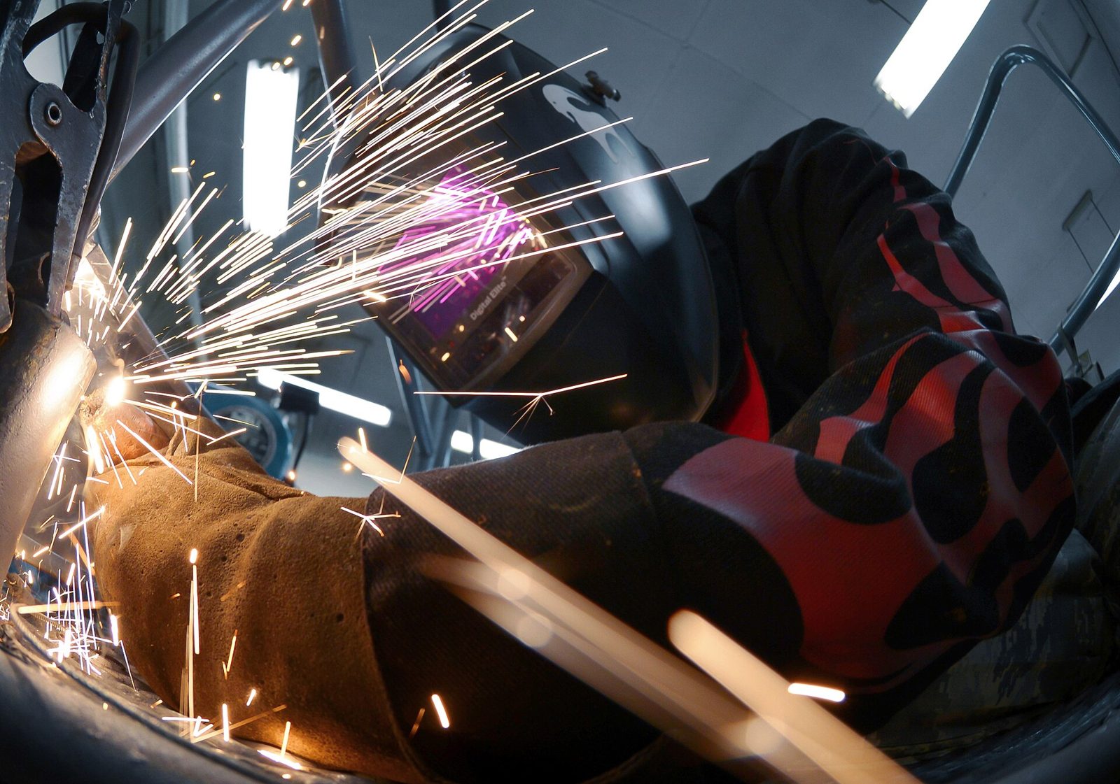 Illustrative welder in protective gear joining steel fabrication inside a workshop